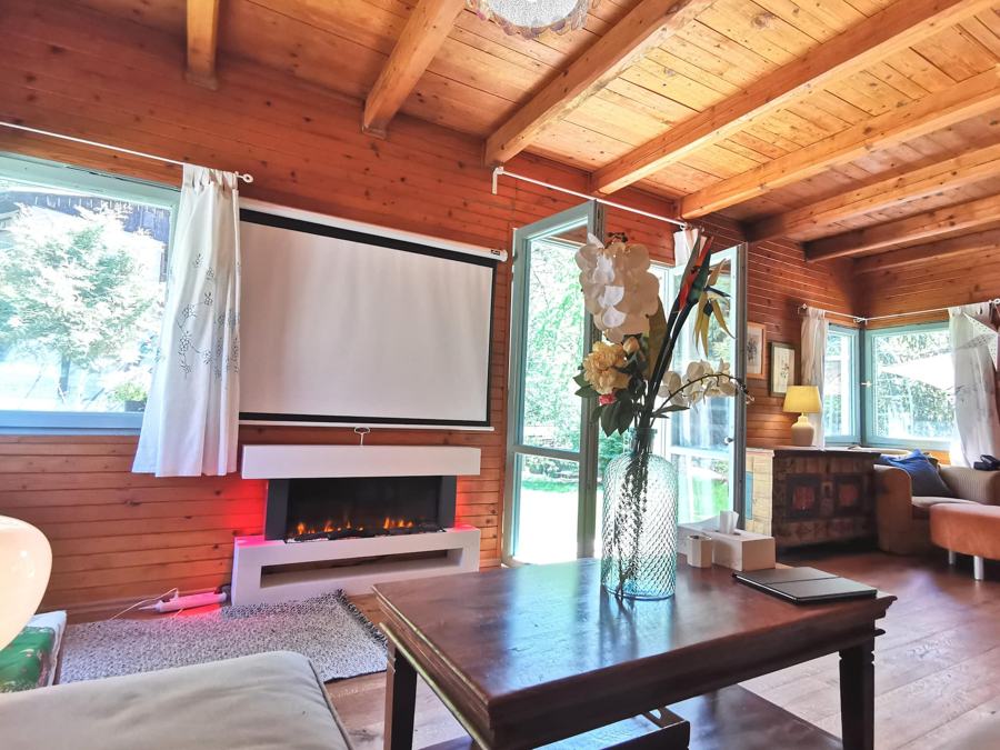 Obývací pokoj s krbem pod oknem, dřevěným stolem a vázou s orchidejí