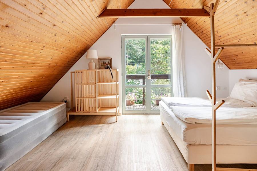 Postele pod šikmým stropem a balkonové dveře do zeleně