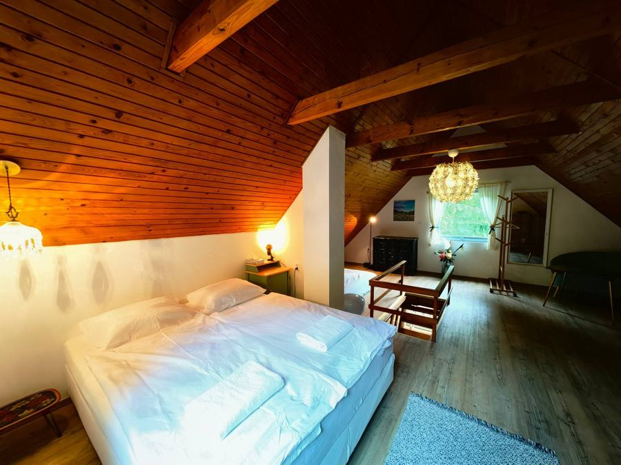 Ložnice pod šikmým dřevěným stropem večer, rozsvícené lampičky