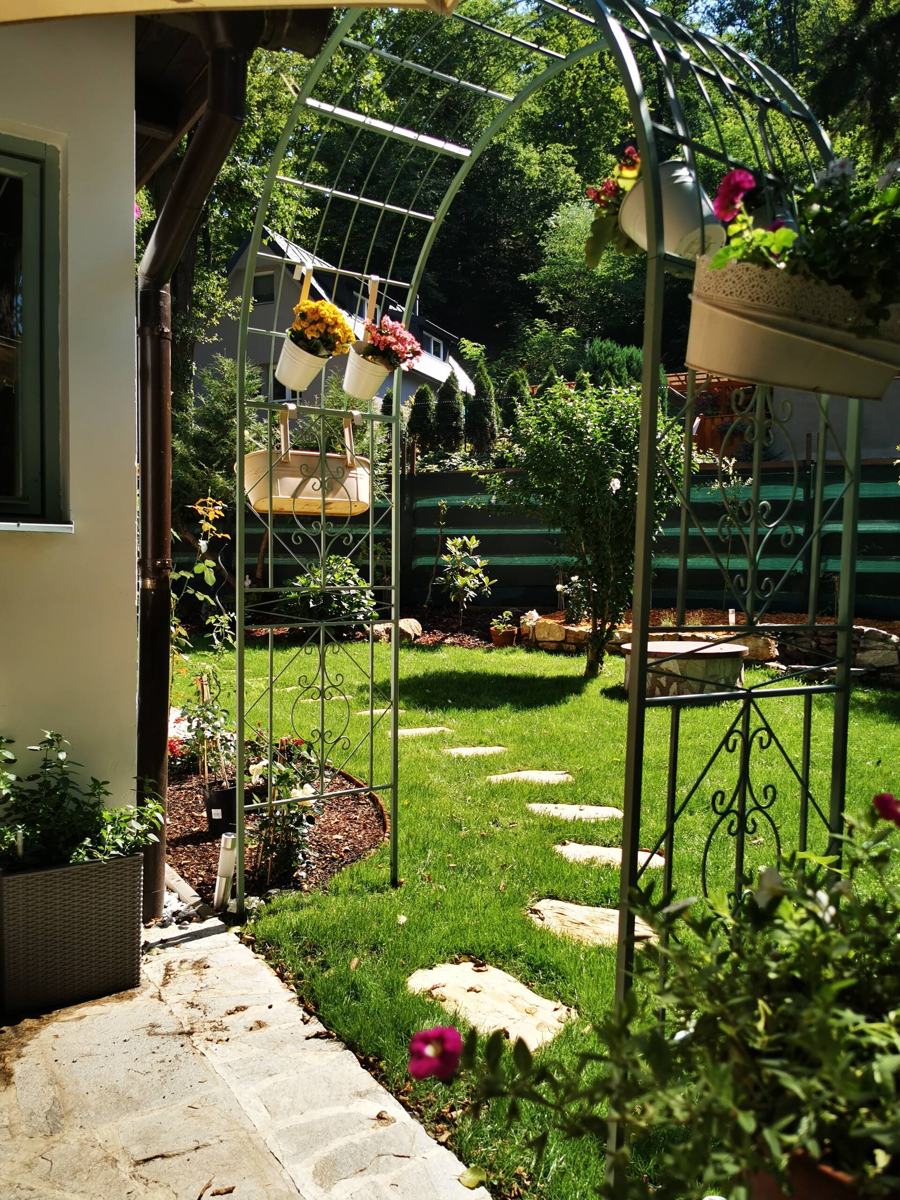 Kovová pergola s květinami a šlapáky v trávě