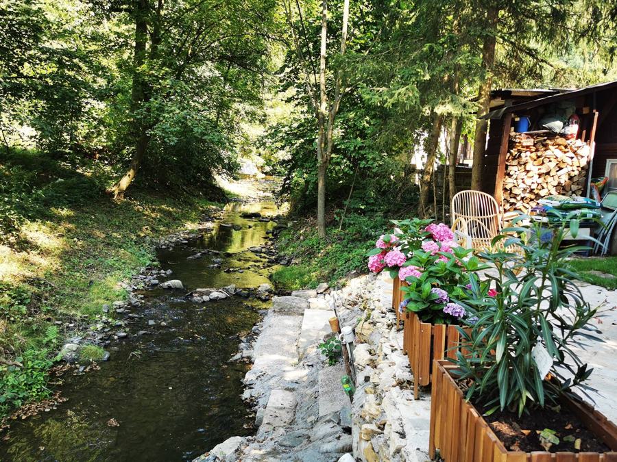 Potok tekoucí kolem kamenné zídky s truhlíky růžových květin
